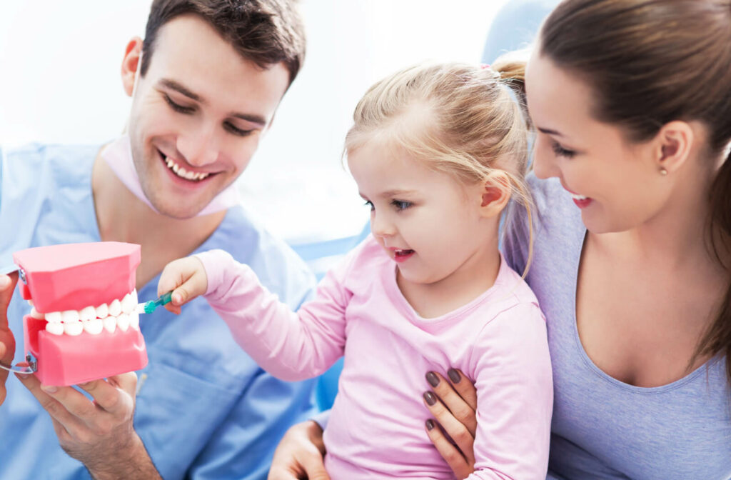 A dentist showing a 3D dental model to a child that is accompanied by her mother.