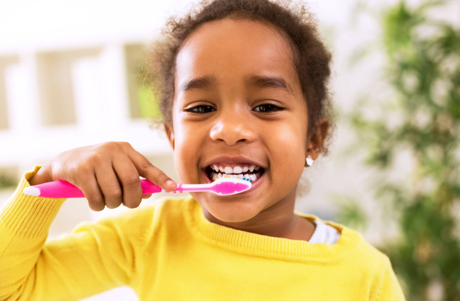 A young girl brushing her teeth using a pink toothbrush.