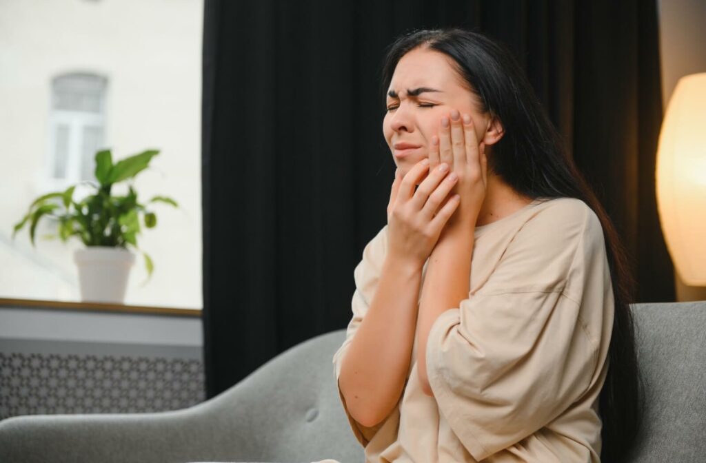 A woman applying pressure to her left cheek to alleviate the pain caused by gum disease.