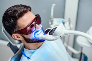 A man with a beard undergoing a teeth whitening procedure that uses ultraviolet light.