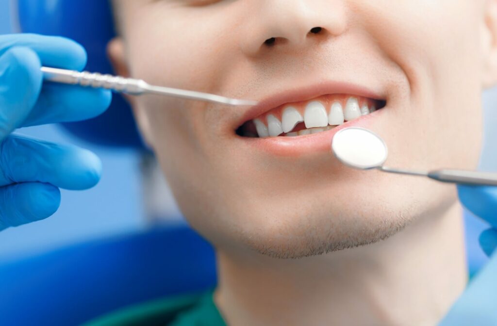 A dentist holds their instruments near a patient's mouth as they prepare to investigate a damaged tooth.