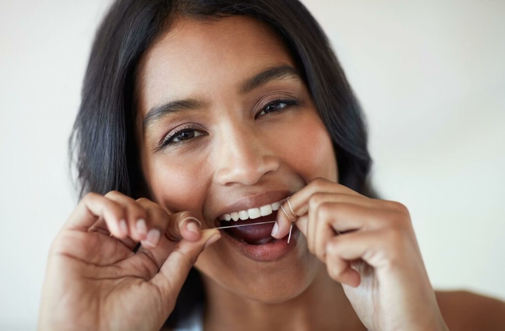 A woman with her mouth open holding floss between her fingers ready to floss her front teeth.
