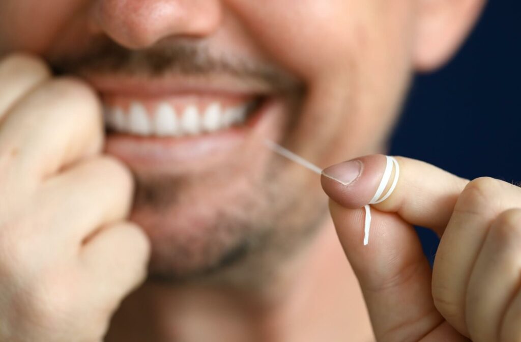 close up of A man practicing good oral hygiene habits and flossing his teeth gently with dental floss.