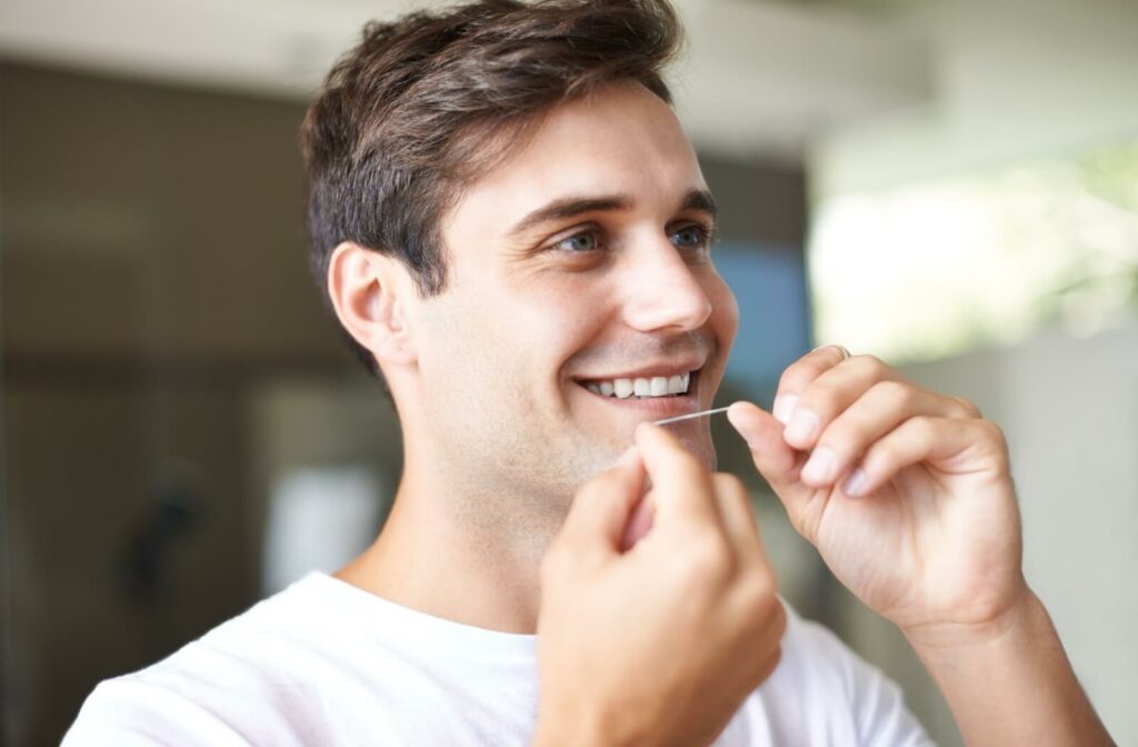 An adult flosses their teeth as part of the personal oral care routine to prevent lengthy dental cleaning appointments.