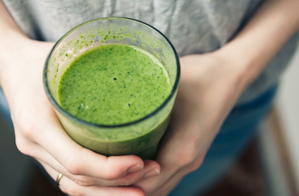 A close up of a green blended smoothie in a glass, held by two hands.