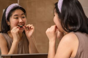 Young woman with long black hair putting in clear mouthguard in the mirror to avoid toothache
