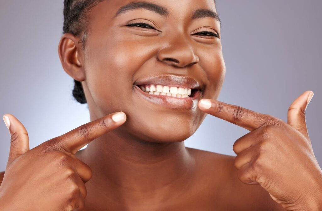 Smiling woman with both hands pointing to white teeth.