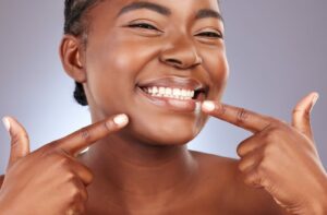 Smiling woman with both hands pointing to whiten teeth.