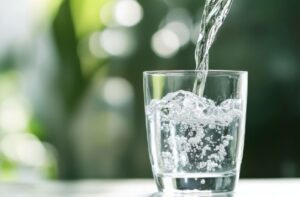 A close-up image of someone out-of-frame pouring water with fluoride into a clear glass.