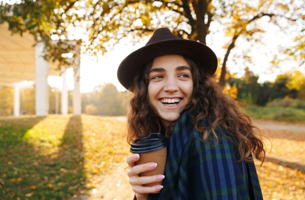 Person smiling outdoors on a sunny autumn day in Toronto while holding a to-go coffee cup.