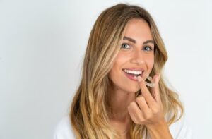 A smiling adult places their clear aligners into their mouth.