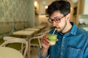 Does Matcha Stain Teeth__supporting 1 | Belman Dental Centre Man drinking iced matcha latte with a straw in a café.