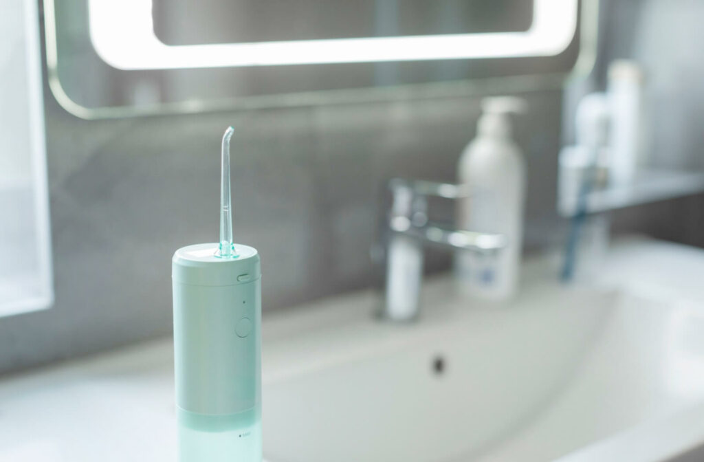A water flosser standing on a bathroom counter with a sink, faucet, and toiletries blurred in the background.