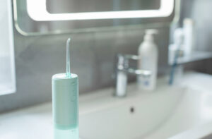 A water flosser standing on a bathroom counter with a sink, faucet, and toiletries blurred in the background.
